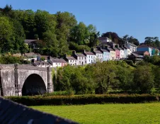 Stone railway viaduct beside a hillside lined with colourful houses and mature trees in Llandeilo, Carmarthenshire, on a clear sunny day.