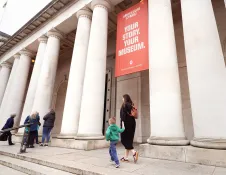 Visitors walking along the steps outside the National Museum Cardiff, with its large stone columns and entrance banners visible