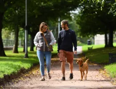 A couple walking a dog along a paved path in a park.
