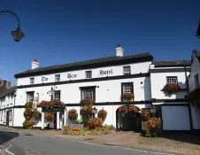 The Bear Hotel, a historic white-fronted hotel decorated with colourful hanging flower baskets, on a sunny street beneath a clear blue sky.