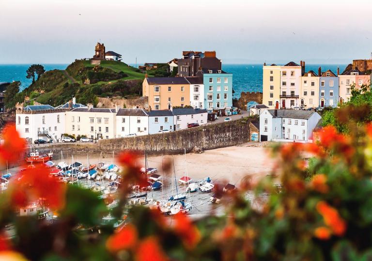 Looking down toward Tenby harbour with boats on the sand and colourful houses and the sea in the background.