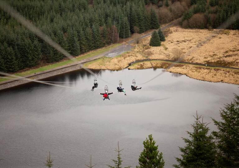 Four people travelling down a zip line above a lake.