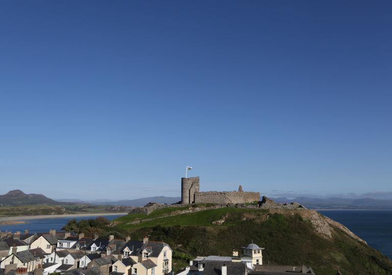 Criccieth Castle on top of a hill from afar, with the sea in the background and houses in the foreground.