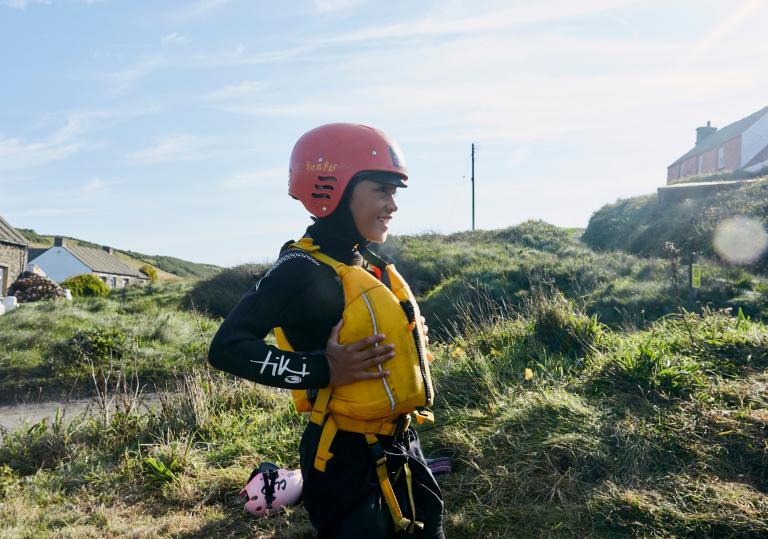 A boy in a yellow life-jacket and red helmet waiting to coasteer in Abereiddy, Pembrokeshire.