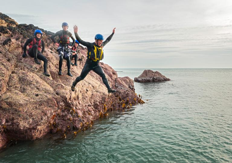 Coasteering group jumping off rocks into sea.
