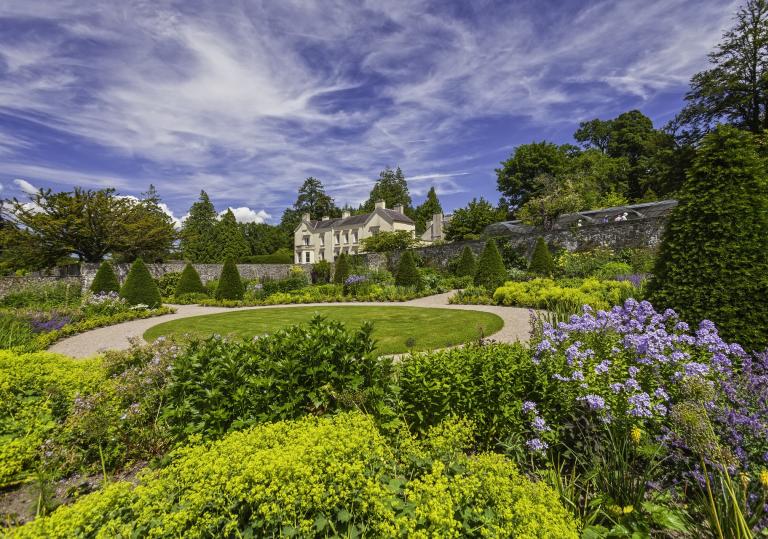 A view of Aberglasney House surrounded by the garden with dramatic blue sky and wispy clouds.