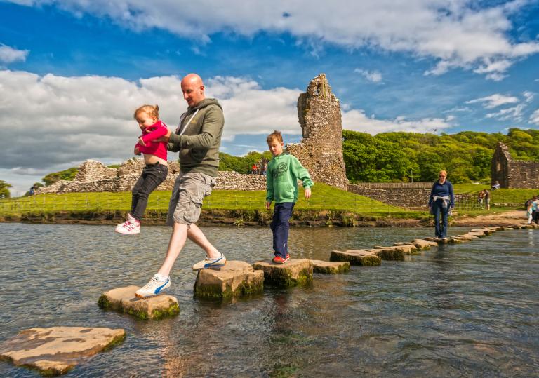 Family walking across stepping stones over Ogmore River.
