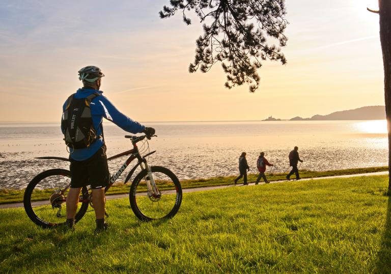 Cyclists on Coast Path at Blackpill at sunrise with Mumbles Head in background