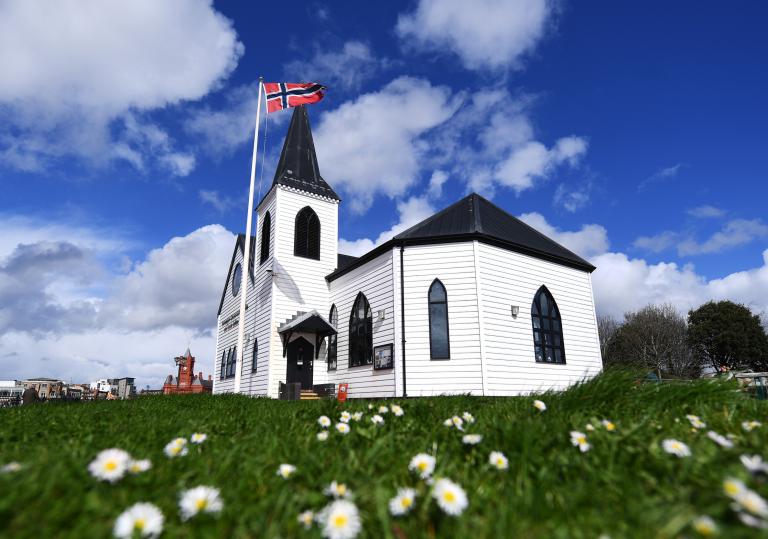 View of the Norwegian Church behind a lawn full of daisies.