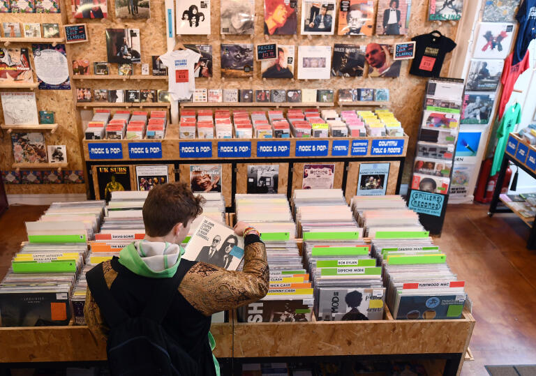A man looking at a tray full of vinyl records inside a record shop.