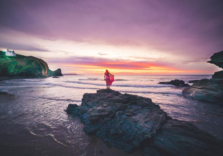 Woman standing on a rock at sunset.