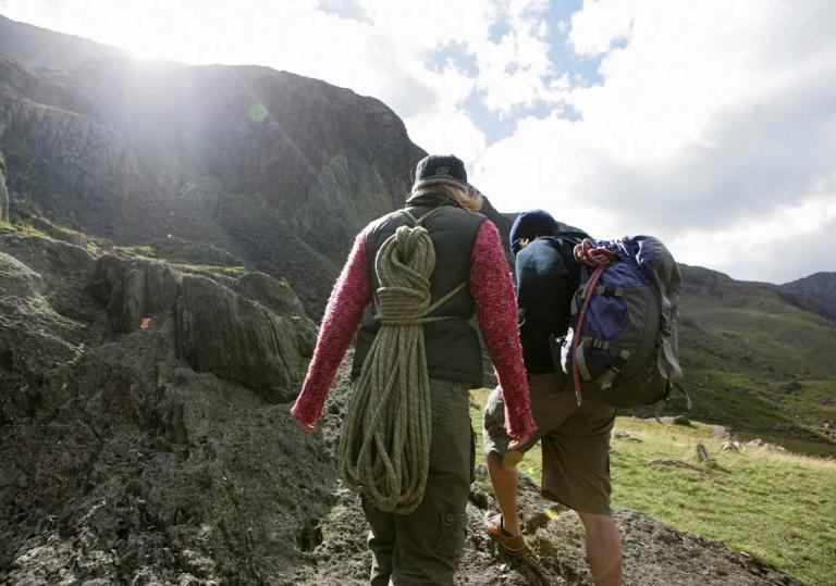 Couple walking towards mountain with ropes on their backs ready to embark on a climb.