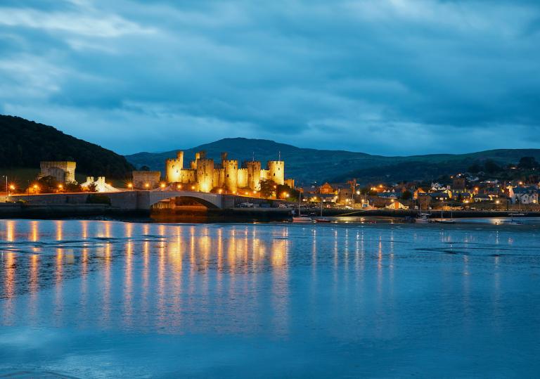Conwy Castle lit up at night and reflection in water.