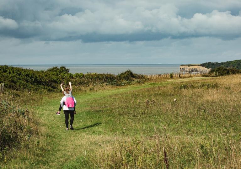 A woman giving a girl a piggy back on a coastal path near Llantwit Major.