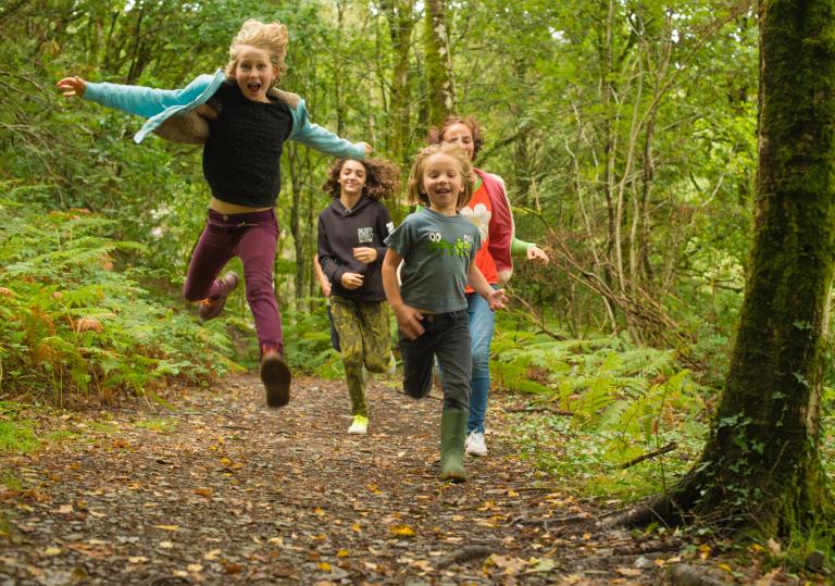 Four children running in woodland.