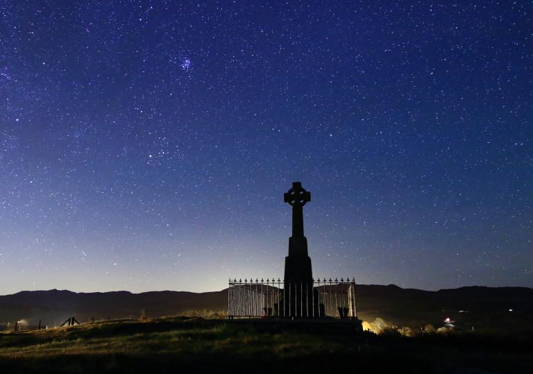 Silhouette of a cross against starry night skies.
