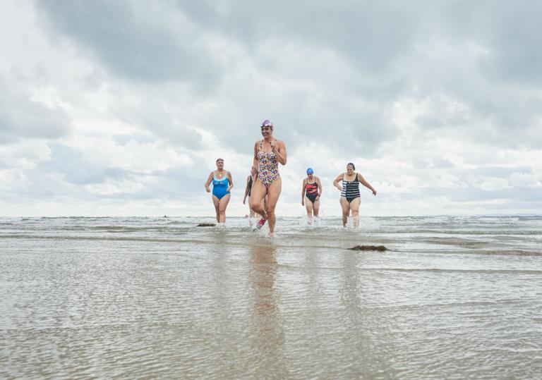 Women in swimming costumes running out of the sea towards the camera.