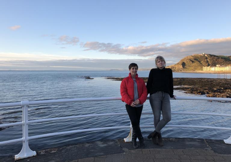 Two women in front of the sea with Constitution Hill in the background.