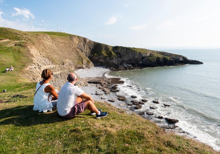Man and woman sat on a clifftop looking out to sea.