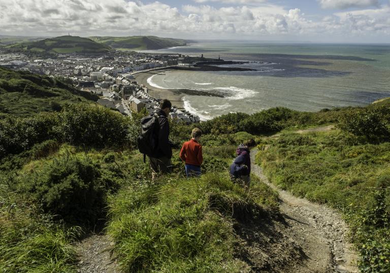 man and two children walking with view towards Aberystwyth coast.