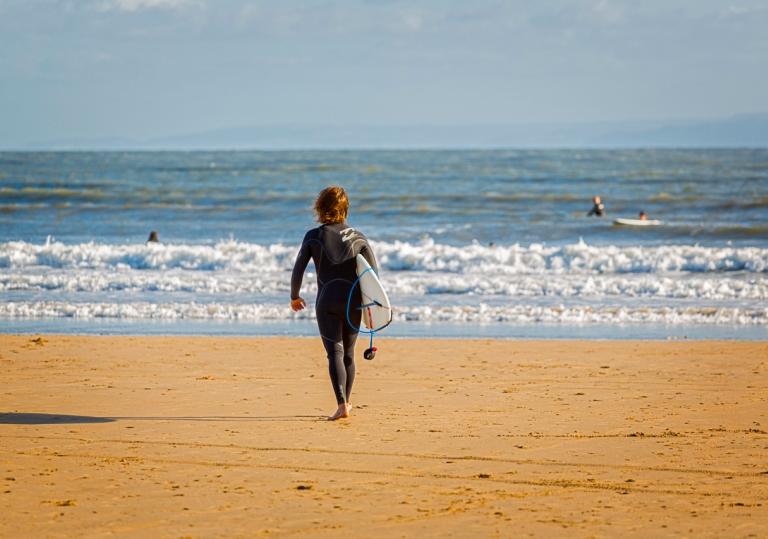 Person walking into the beach with a board at Porthcawl beach