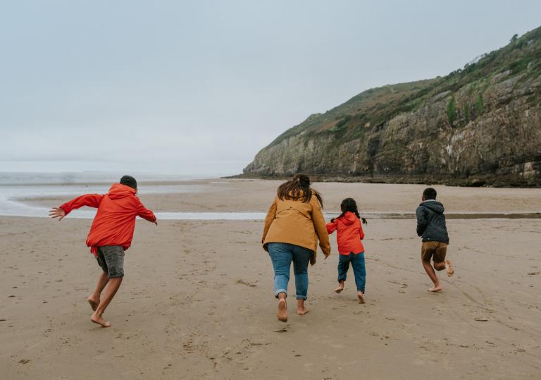 An adult and three children running on a beach.
