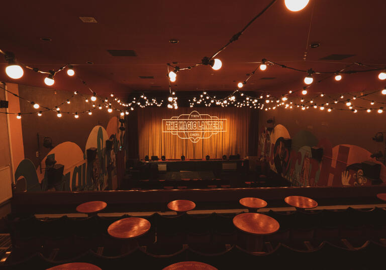 Inside the Magic Lantern cinema, with round wooden tables, cinema chairs and festoon lighting. 