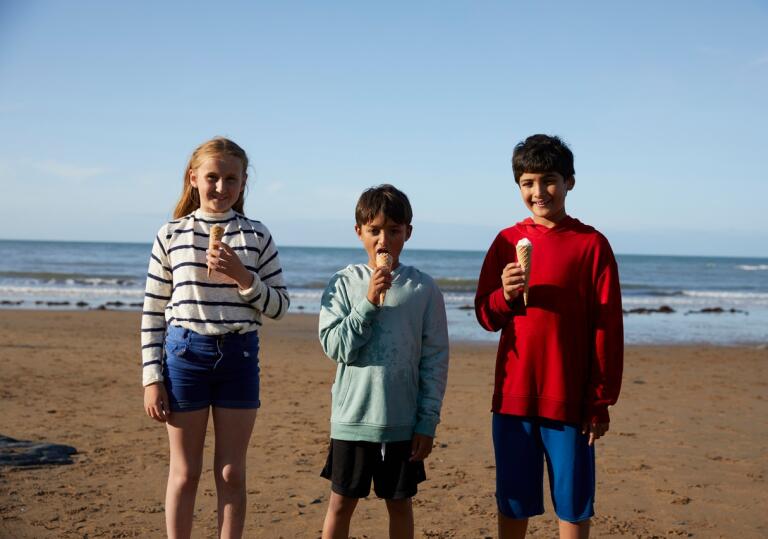 Three children standing on a beach on a sunny day eating ice cream 