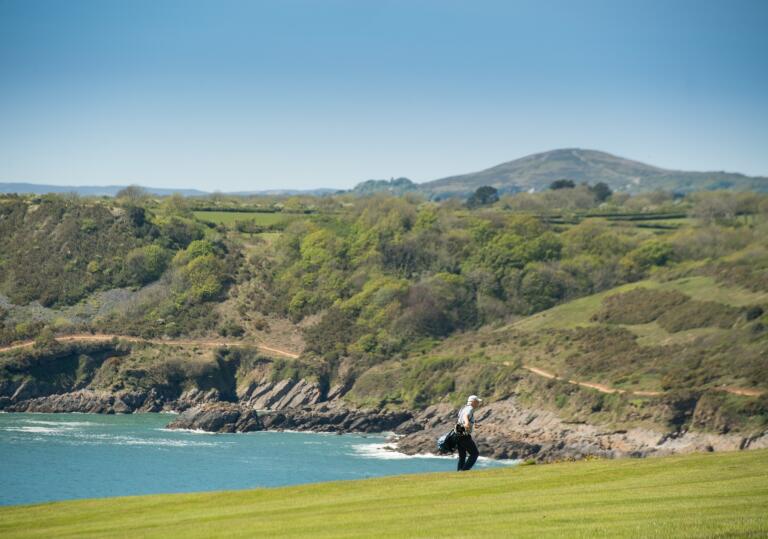 Man playing golf on a clifftop overlooking a bay