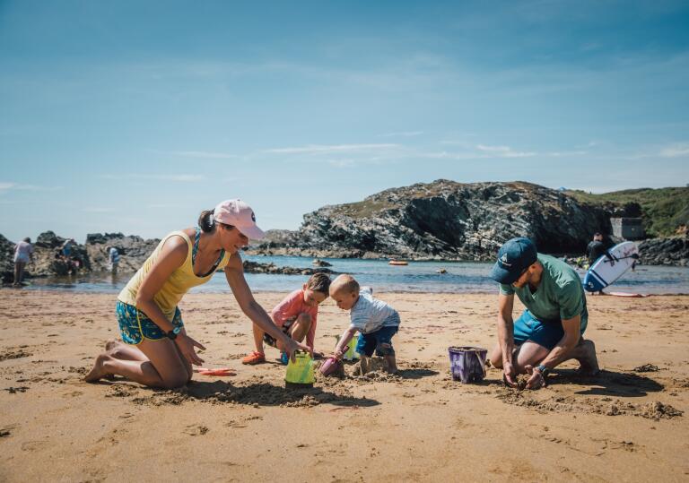 Two adults and two young children building sandcastles on a beach.