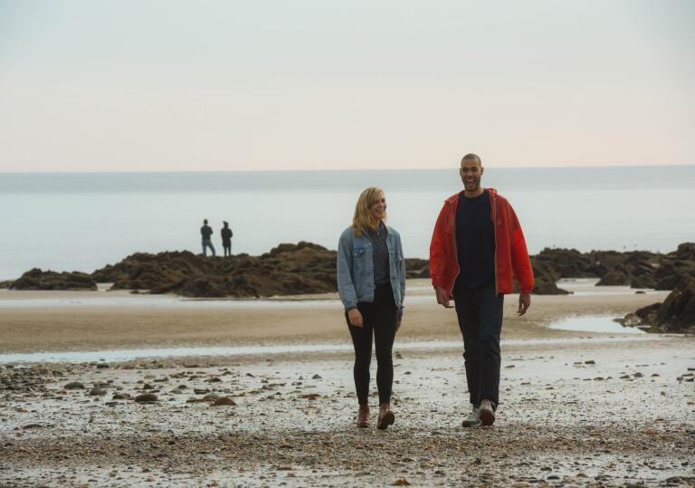 Couple walking on Saundersfoot beach with another couple standing on rocks in the distance