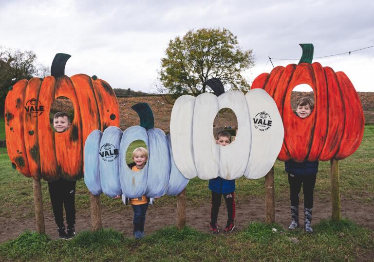 children inside pumpkin cut outs posing for photo.