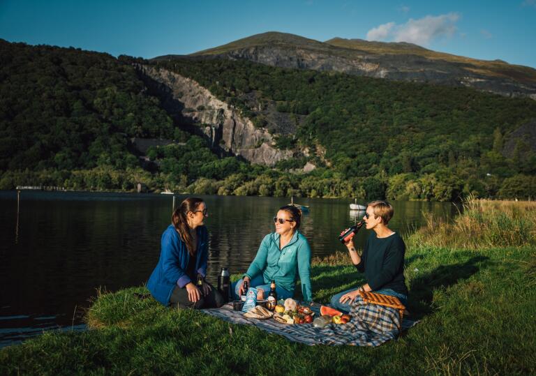 three woman having a picnic by lake.