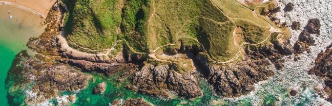 An aeriel shot of the Wales Coast path on a rocky cliff against the sea water.