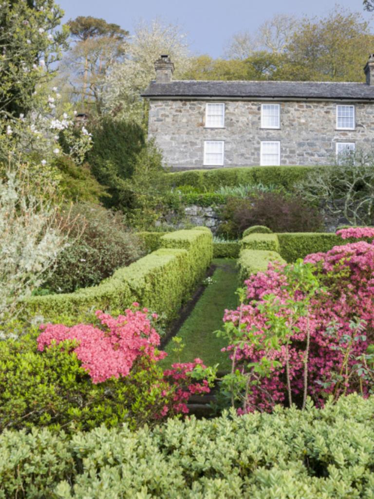 Garden in foreground with pink flowers and hedges with Plas yn Rhiw house in background.