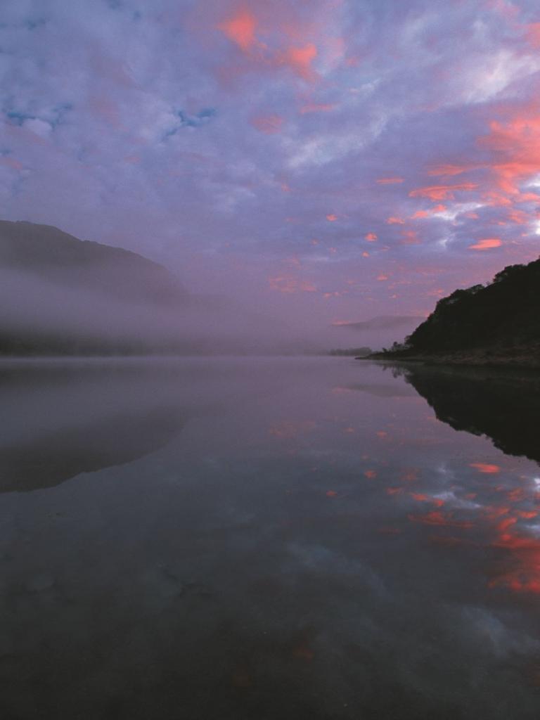 Red sky, mountains and clouds reflecting on the water at Llyn Dinas, Snowdonia.