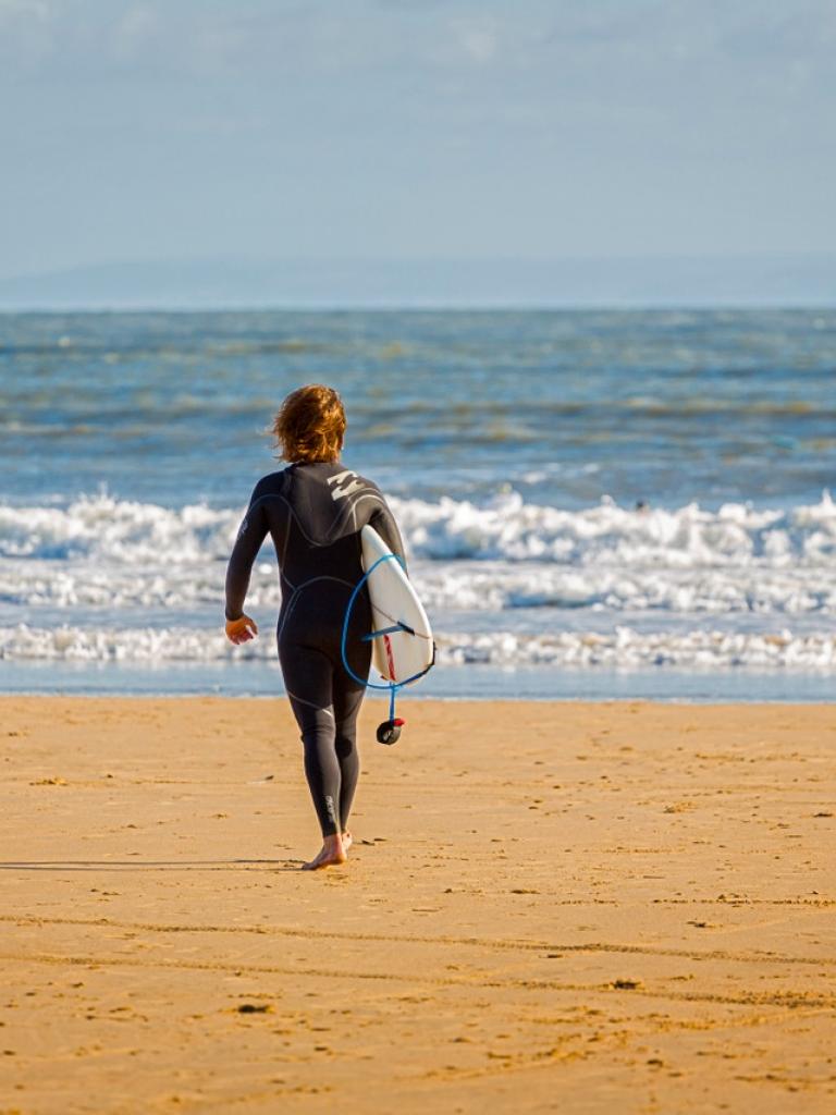 Person walking into the beach with a board at Porthcawl beach