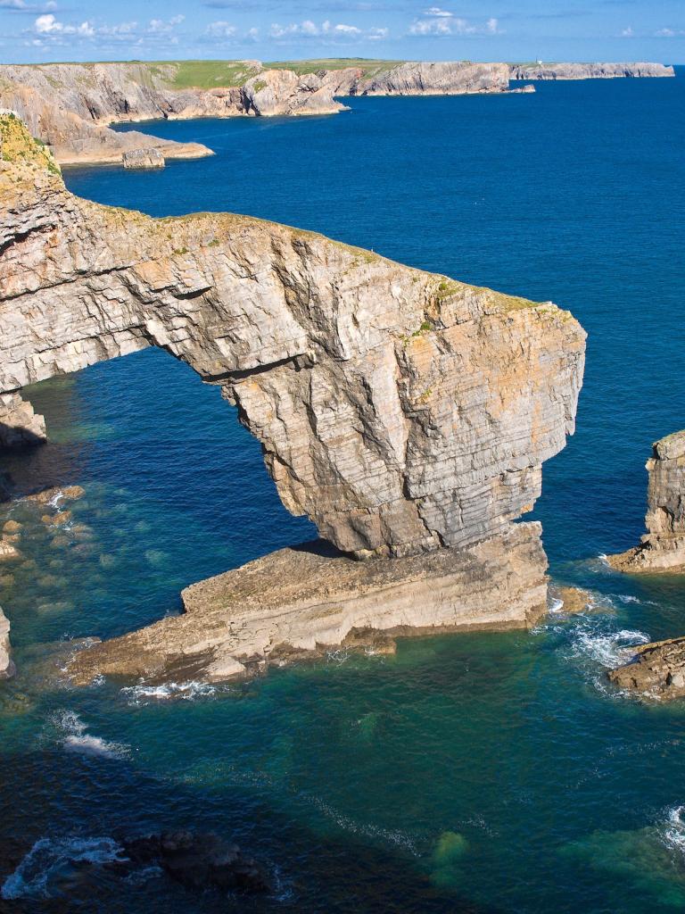 Green Bridge of Wales rock formation surrounded by blue sea.
