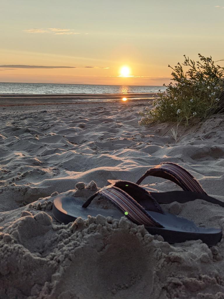 Sonnenuntergang am Strand mit Flip Flops im Vordergrund.