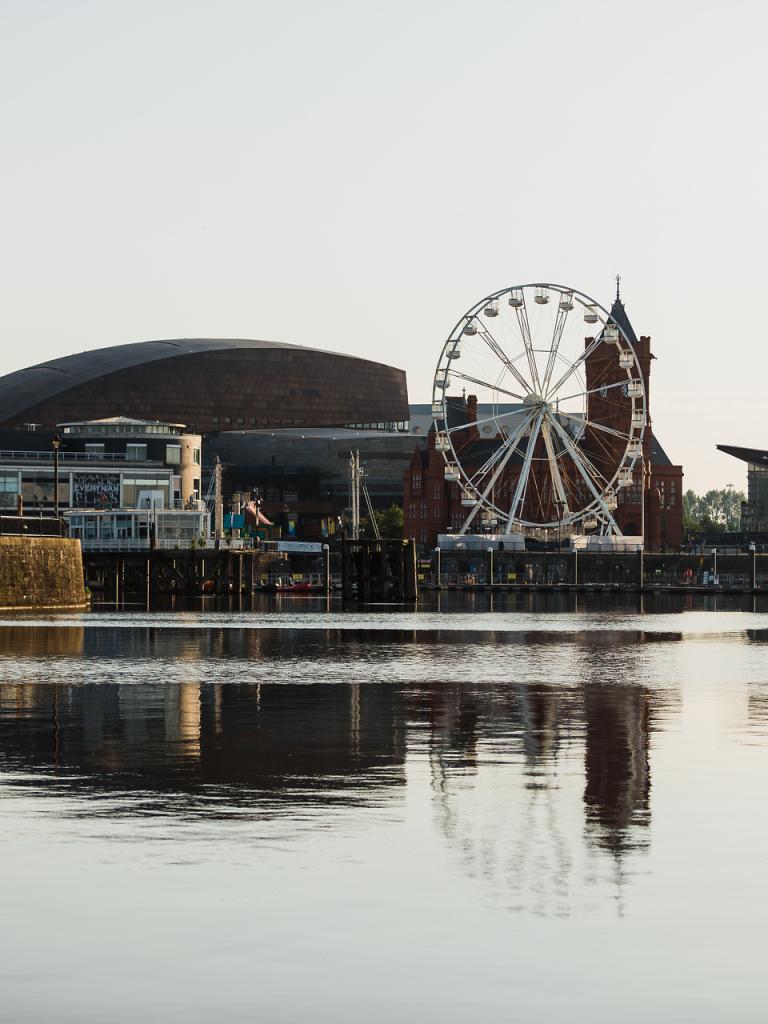 A view of Cardiff Bay from the water showing buildings and a big wheel