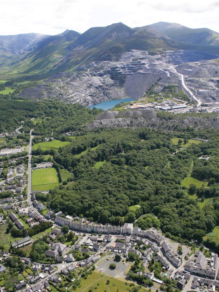 Aerial photo of the Bethesda and Penrhyn quarry area. There are a number of fields and woodland between a densely populated area of houses and the mountainous landscape of the quarries.