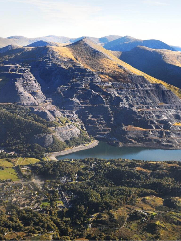 A mountainous slate quarry landscape with a blue pond in the middle.