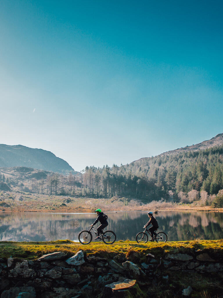 Two people riding mountain bikes on a lakeside trail.