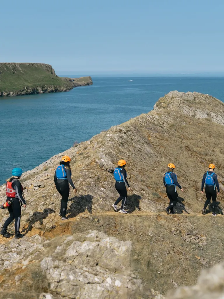 A kitted up group walking along a cliff path ready to go coasteering.