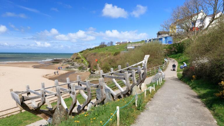Wooden boat skeleton sculpture alongside the coast path with sandy beach in the background