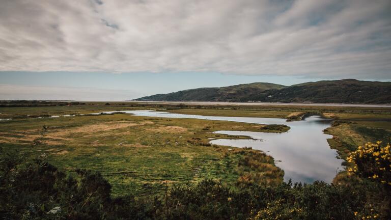 Dyfi estuary with grass on each side and hills in the background under moody skies