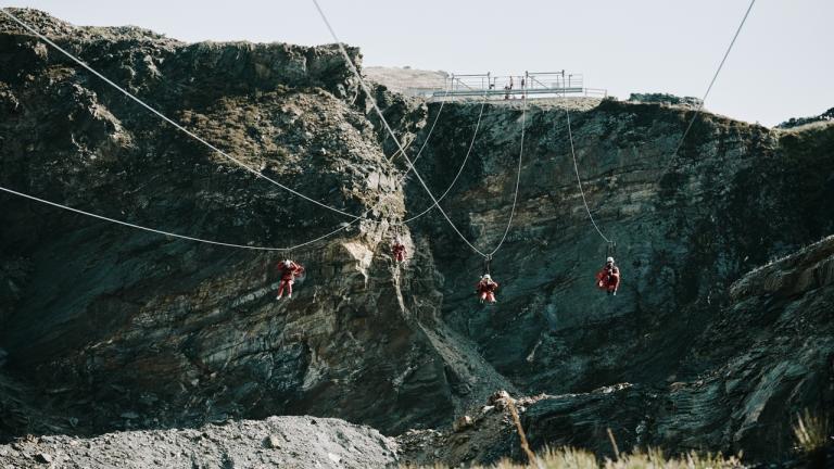 Four people on a seated zip wire travelling down from a slate quarry.