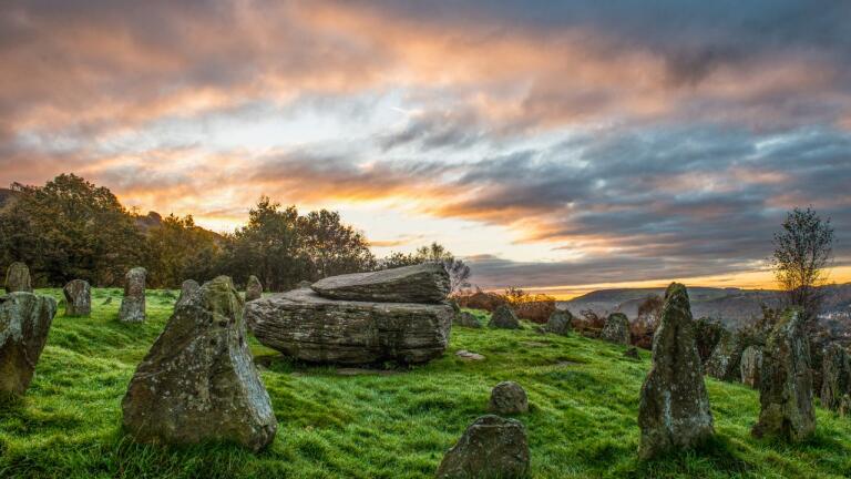 Pink sky sunrise over ancient standing stones on a green hillside