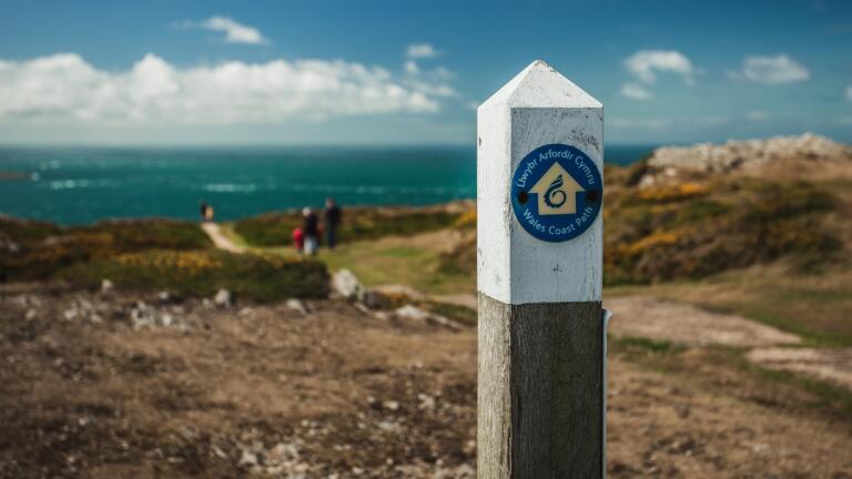 Wales Coast Path signpost with coast, path and sea in the background.