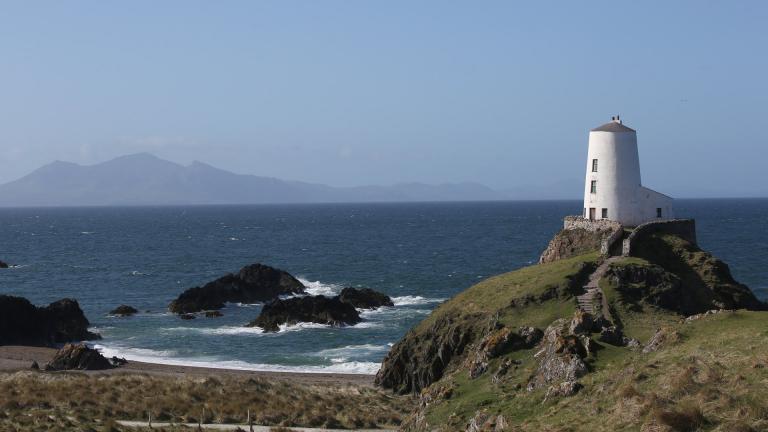 View looking out to sea with white lighthouse in foreground, Llanddwyn Island, North Wales